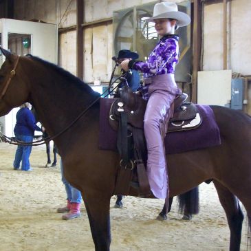 Young girl riding a horse indoors, dressed in western attire.