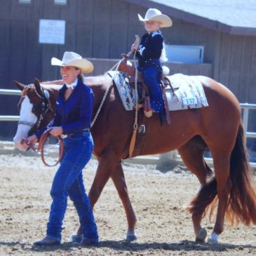 Child riding a horse with adult leading it outdoors.