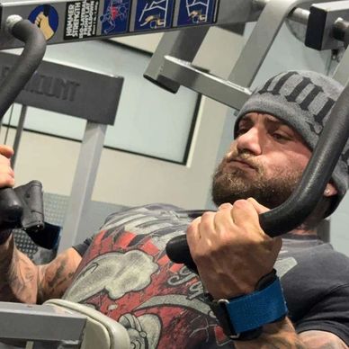 Man focused on chest workout using gym machine, wearing a beanie and wrist support.