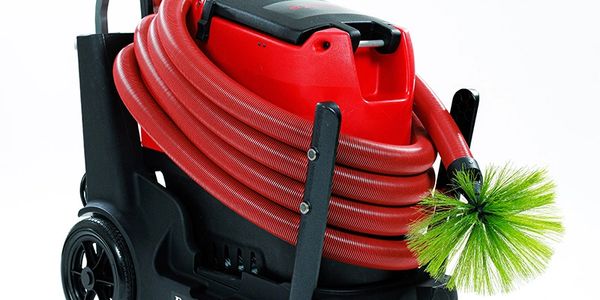 A red hose coiled on a black wheeled cart with a green brush attached.