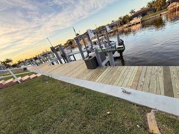 Wooden dock extending over calm waterfront with houses and palm trees at sunset.