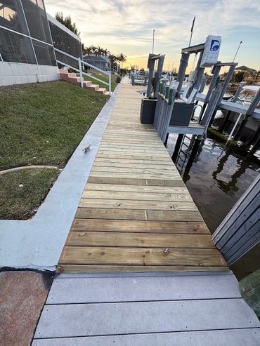 Wooden dock pathway beside water and grassy area at sunset.