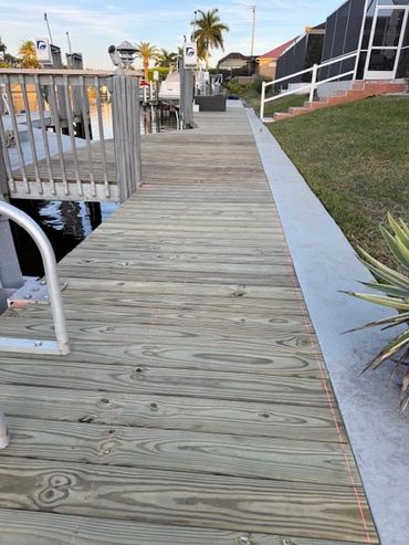 Wooden boardwalk along a waterfront with palm trees and docks.