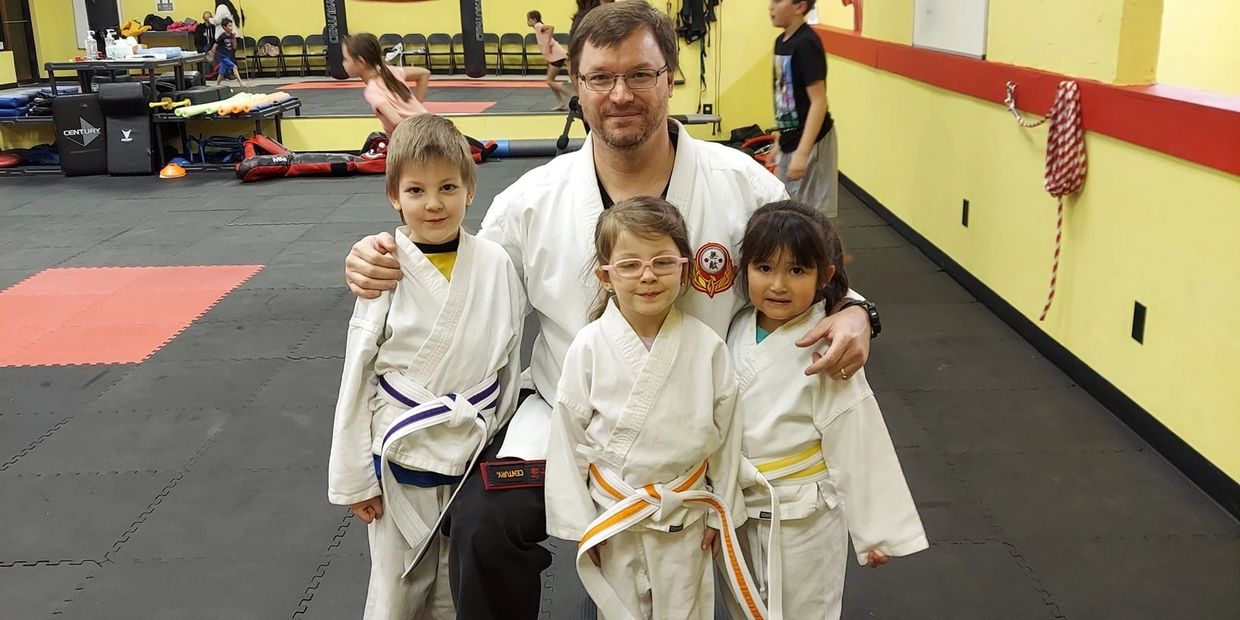 Martial arts instructor with three children in karate uniforms posing in a dojo.