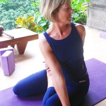 Woman practicing seated yoga twist pose on a mat outdoors.