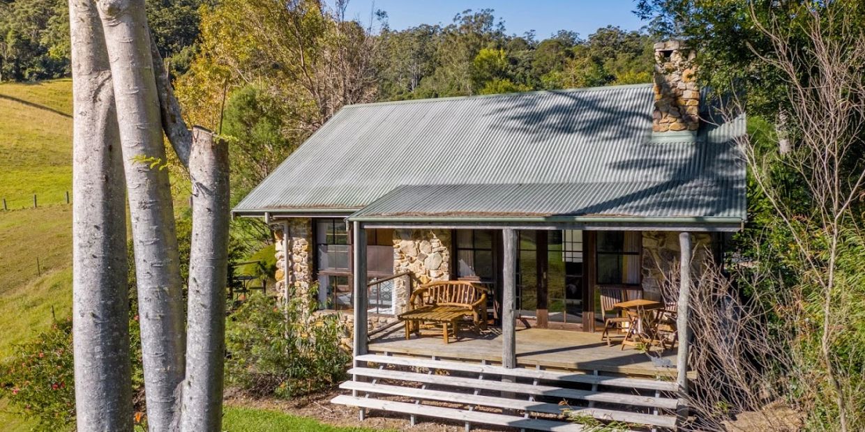 Cozy stone cottage with wooden porch furniture surrounded by nature.