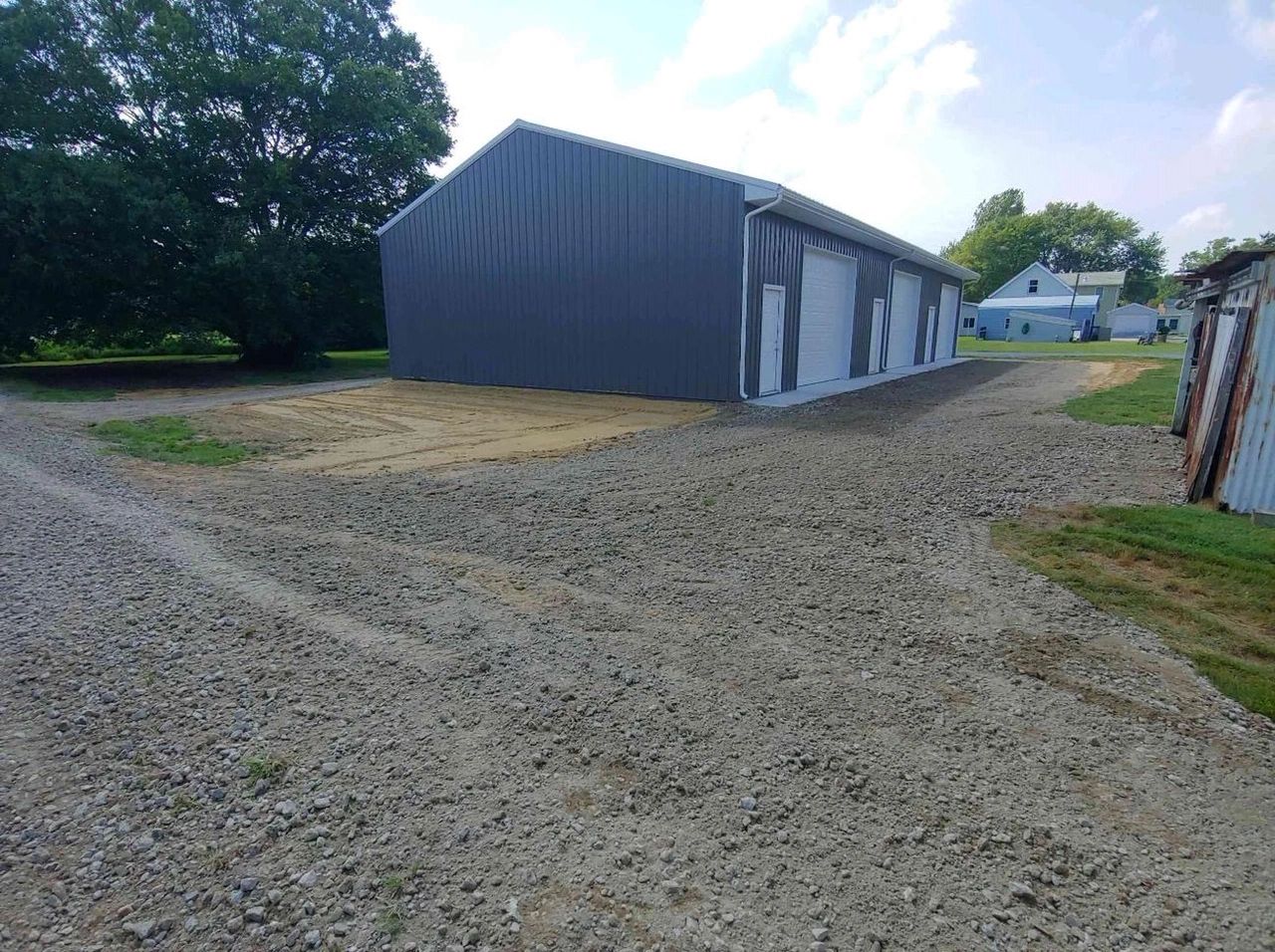 A large gray metal building with gravel and dirt driveway.