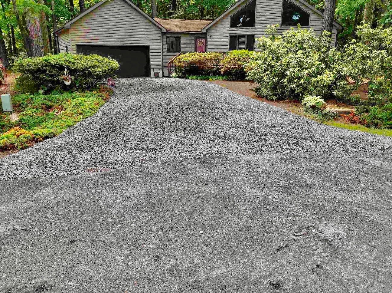 Newly laid gravel driveway leading to a modern house surrounded by greenery.