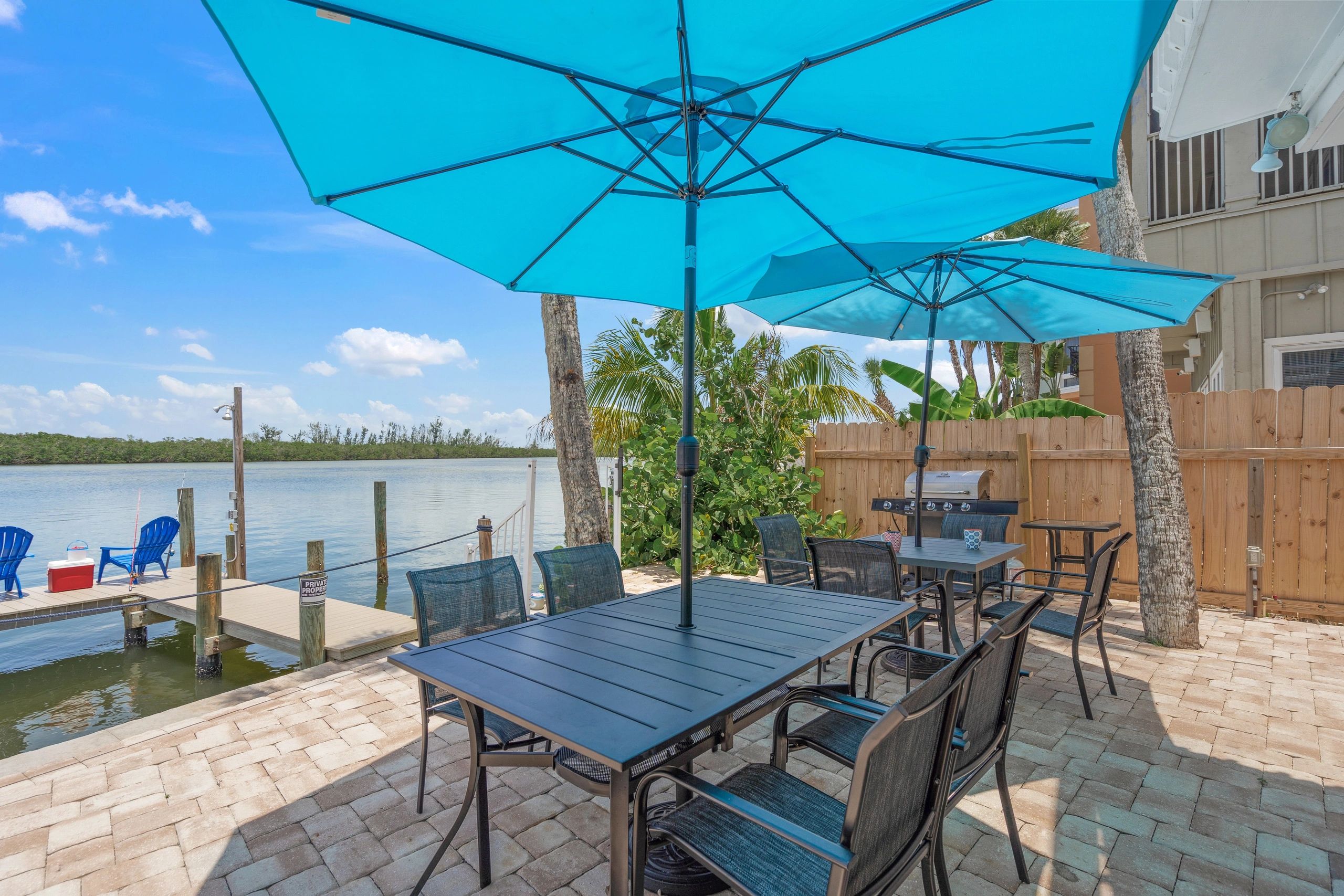A patio area with outdoor tables and blue umbrellas overlooking the water.