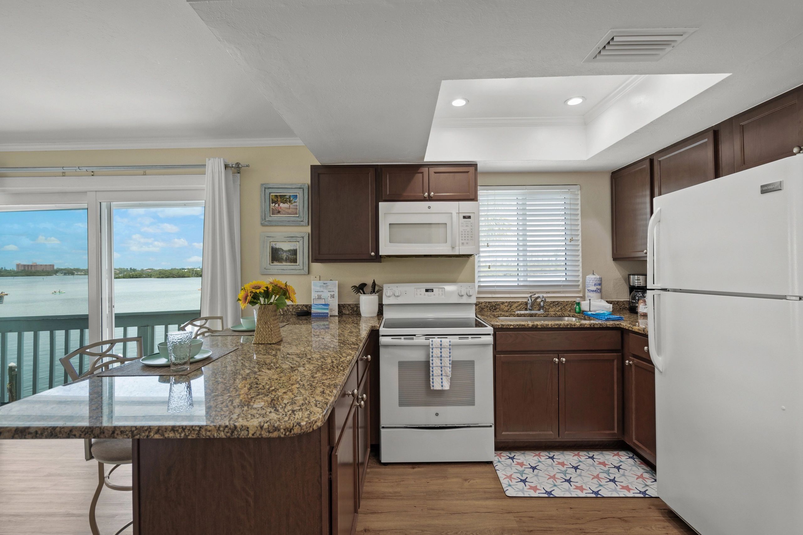 A kitchen with a granite countertop, white appliances, and a view of the balcony.