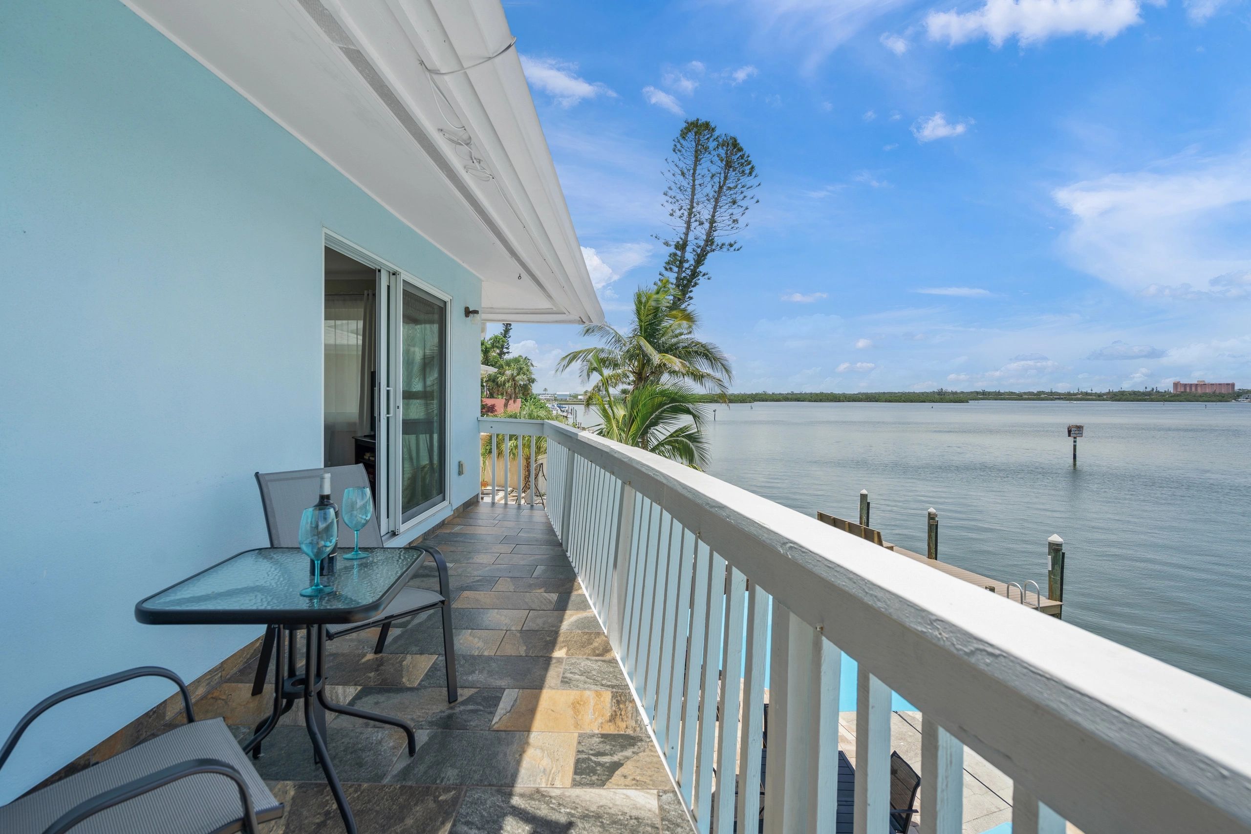 A balcony with a glass table and chairs overlooking the water.