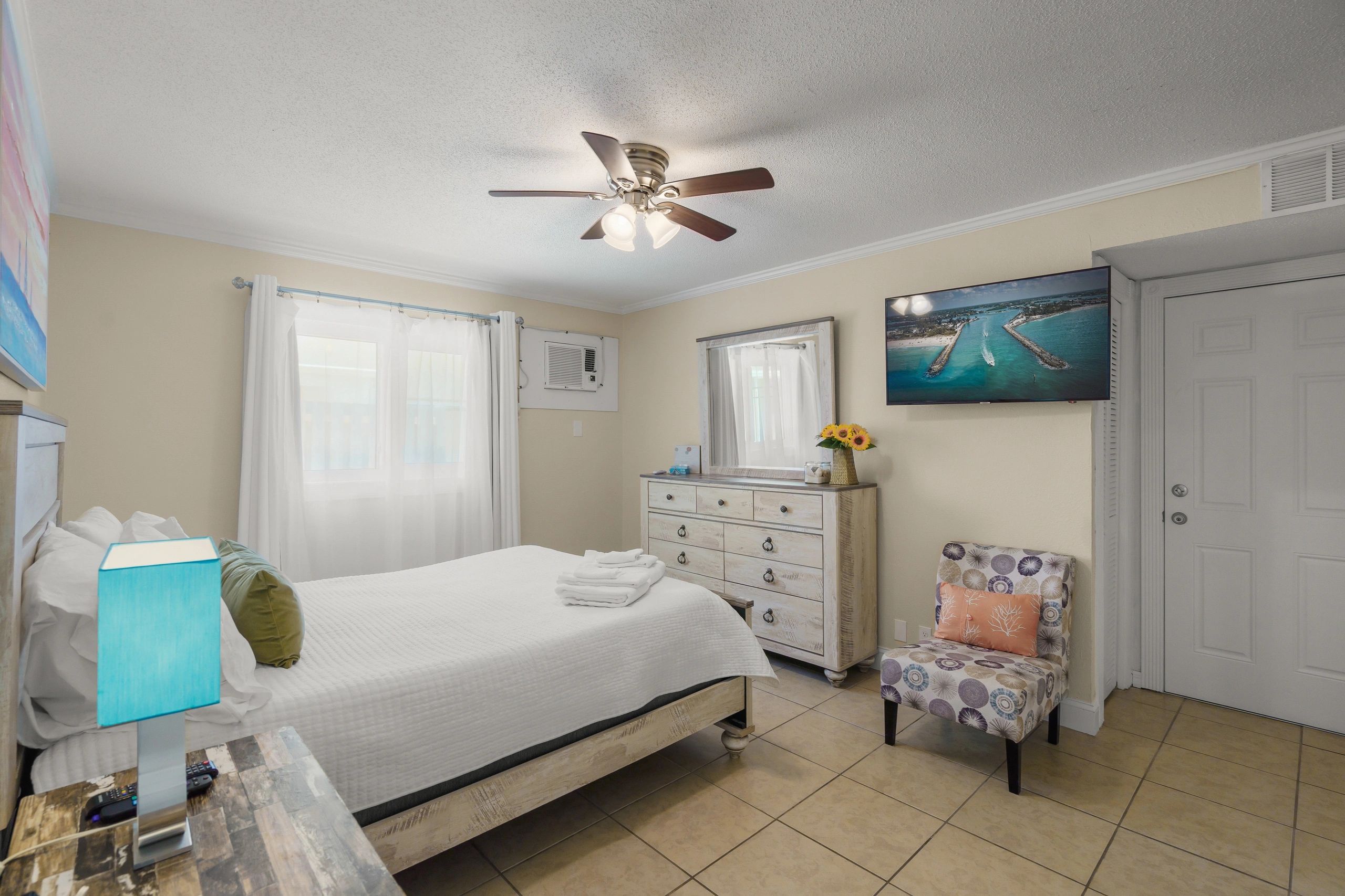 A wide-angle view of a guest room with a bed, dresser, chair, and TV.