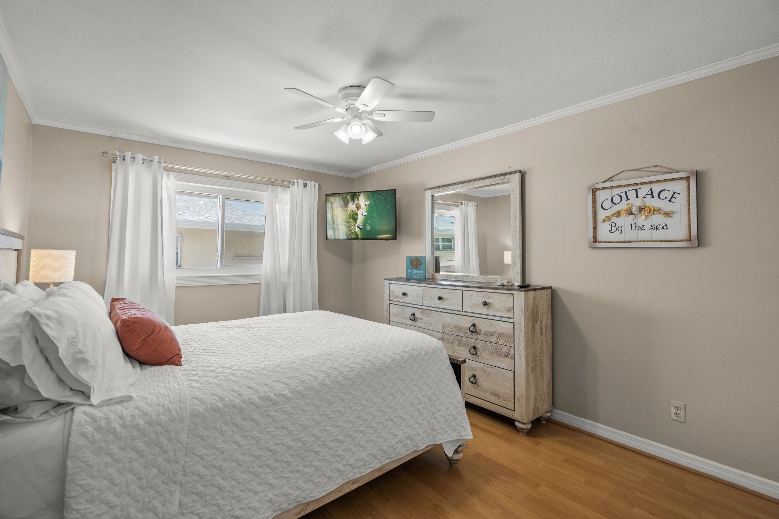 A wide view of a guest room with a bed, dresser, mirror, and TV.