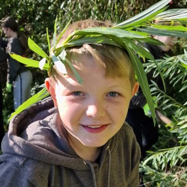 Boy with a leafy crown smiling outdoors.