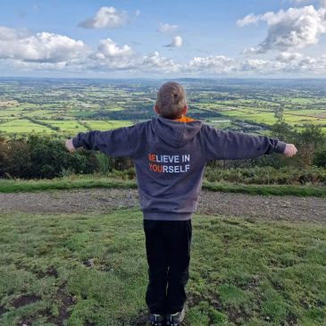 Person with outstretched arms overlooking a green landscape.