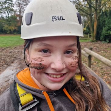 Smiling girl with a helmet and mud on her face.