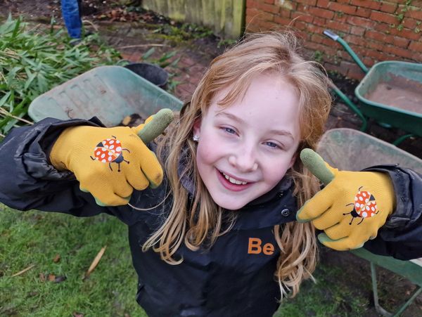 Smiling girl giving thumbs up in garden gloves.