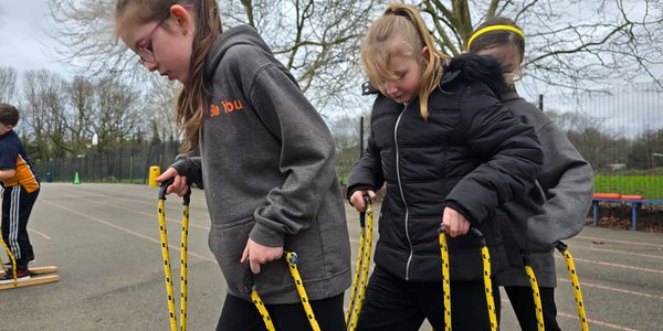 Three children coordinating on a rope-walking activity outdoors.