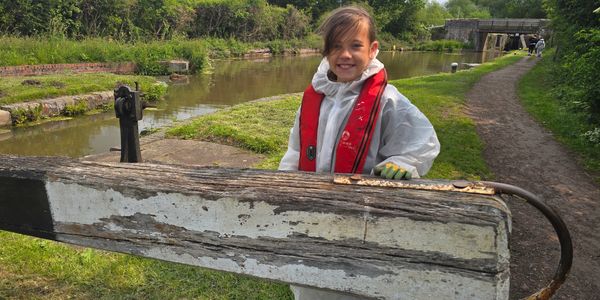 Child smiling by canal lock gate wearing life jacket.