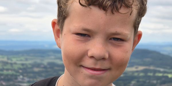 Close-up of a boy smiling outdoors with a scenic background.