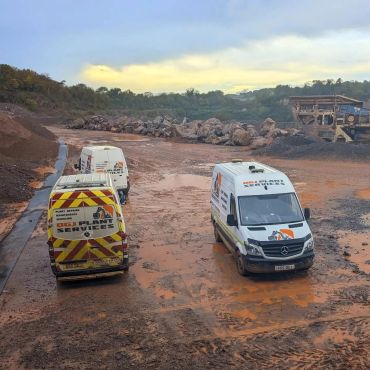 Service vans parked on a muddy construction site with rocks and machinery.
