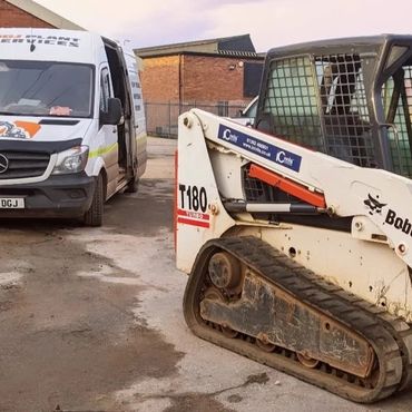 Bobcat T180 skid-steer loader parked near a white van in an industrial area.
