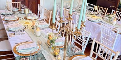 Elegant dining table set with white chairs, candles, and floral centerpieces.