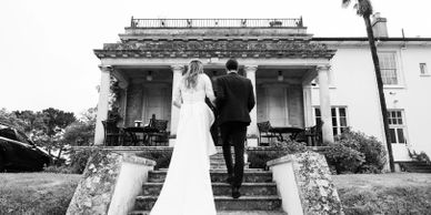 Black and white photo of a bride and groom walking up steps to a large building.