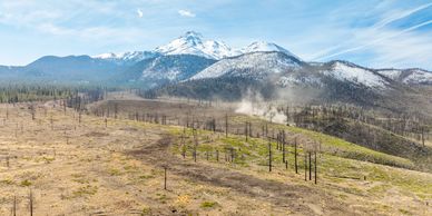 A mountainous landscape with snow-capped peaks and burnt forest areas.