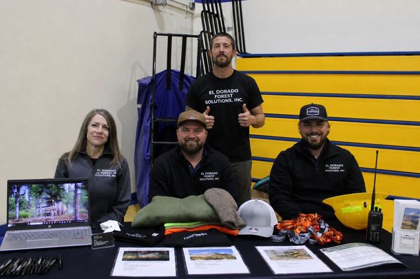 Three people at a booth for El Dorado Forest Solutions, Inc. with promotional items.