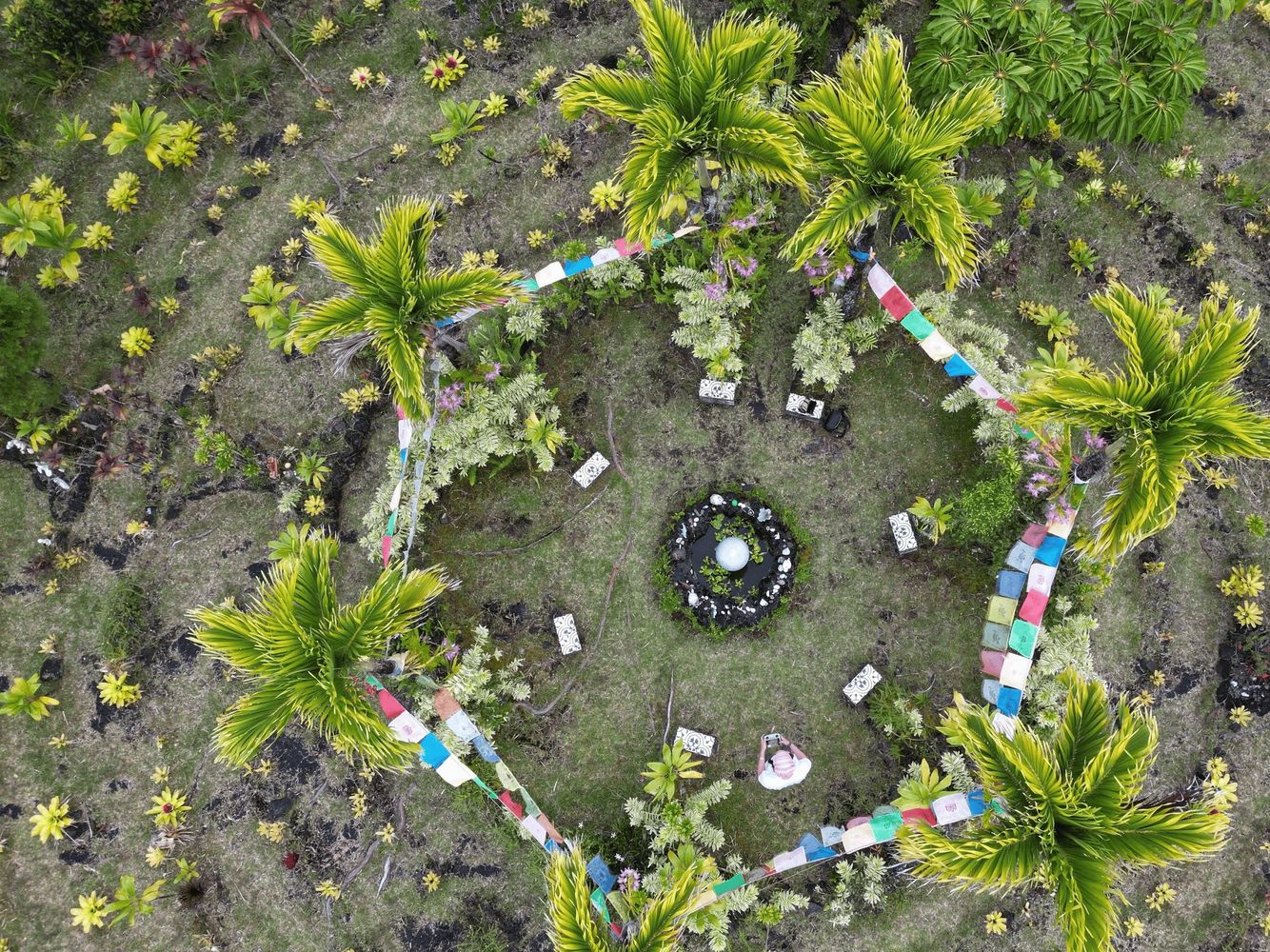 Aerial view of a circular garden with palm trees and colorful flags.