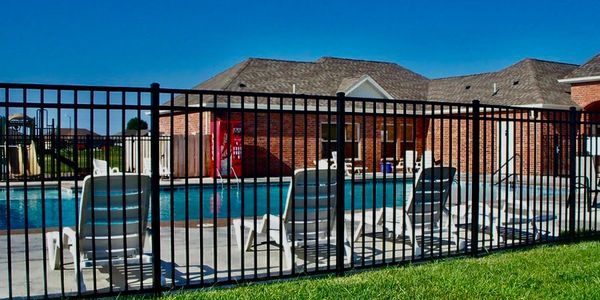 Outdoor pool area with lounge chairs behind a black metal fence.