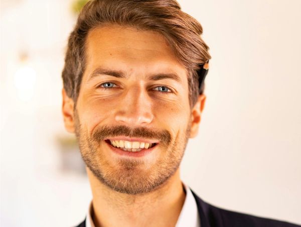 Smiling man with light brown hair and beard in formal attire.