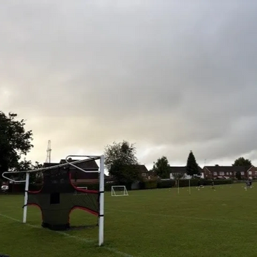 A sports field with soccer goals and houses in the background under a cloudy sky.