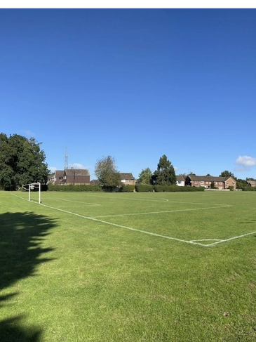 Empty soccer field under a clear blue sky with houses in the background.