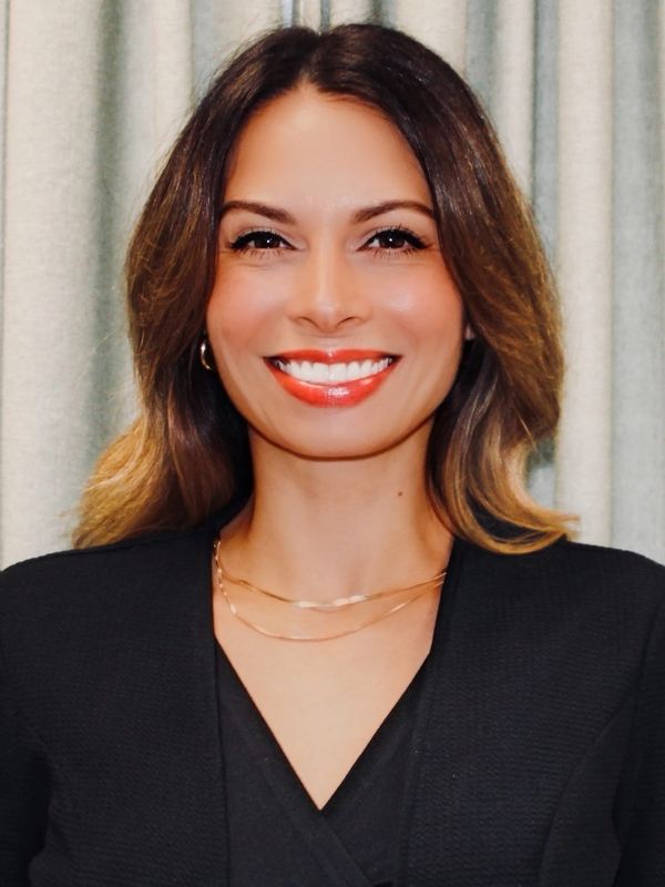 Smiling woman with wavy hair wearing black and gold jewelry.