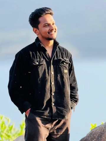 A young man smiling outdoors with hands in pockets.
