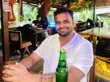 Man smiling at a restaurant table with a drink.