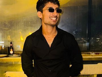 Smiling man in black shirt and sunglasses indoors.