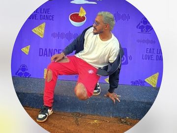 Man sitting casually against a vibrant purple wall.