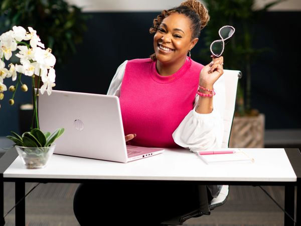 Smiling woman in pink sweater working at a laptop.
