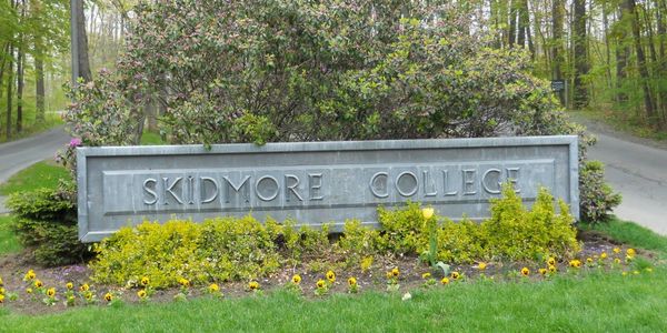 Stone sign for Skidmore College surrounded by flowers and greenery.