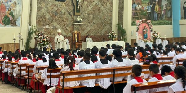 Children attending a church service with a priest speaking at the altar.