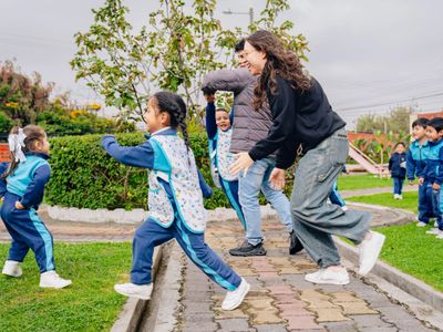 Children and a teacher joyfully running outdoors in a school playground.