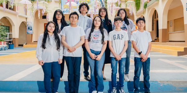 A group of nine teenagers posing together outdoors at a school courtyard.