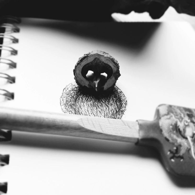 A walnut half on a sketchpad with drawn hair and a wooden key nearby.