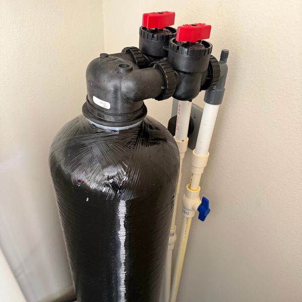 Black water softener tank with red valve handles.
