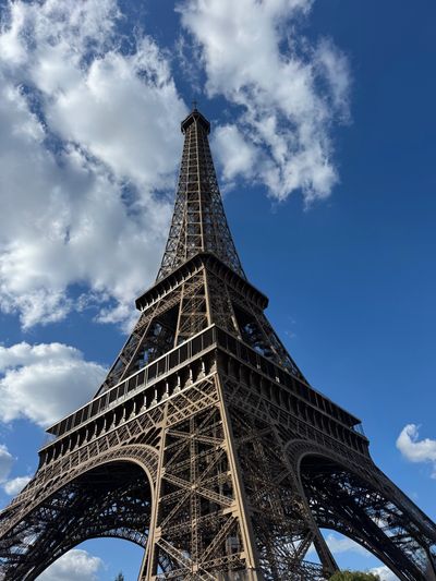 View looking up at the Eiffel Tower against a blue sky with clouds.