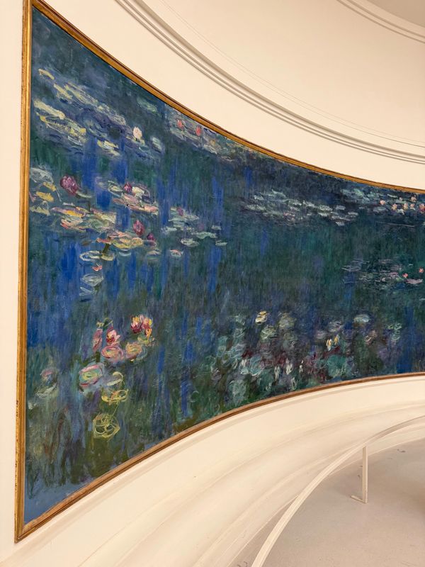 Curved painting of water lilies with a white bench in front.