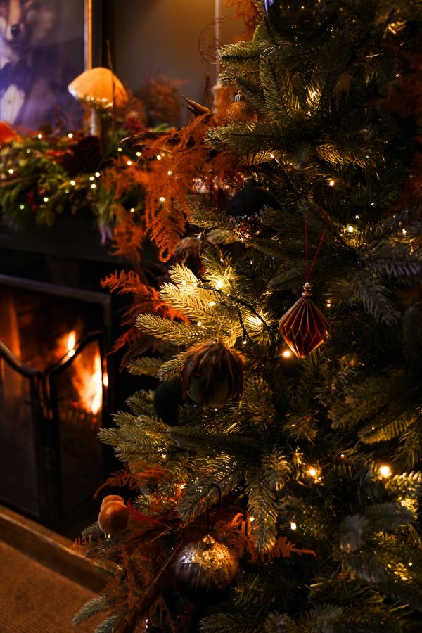 Cozy Christmas tree with warm lights near a fireplace.